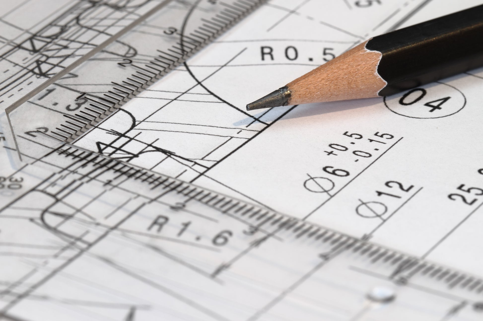 Auf dem Bild ist eine technische Zeichnung mit Maßangaben und Maßlinien zu sehen. Auf der Zeichnung liegt ein Bleistift und ein dreieckiges Lineal.