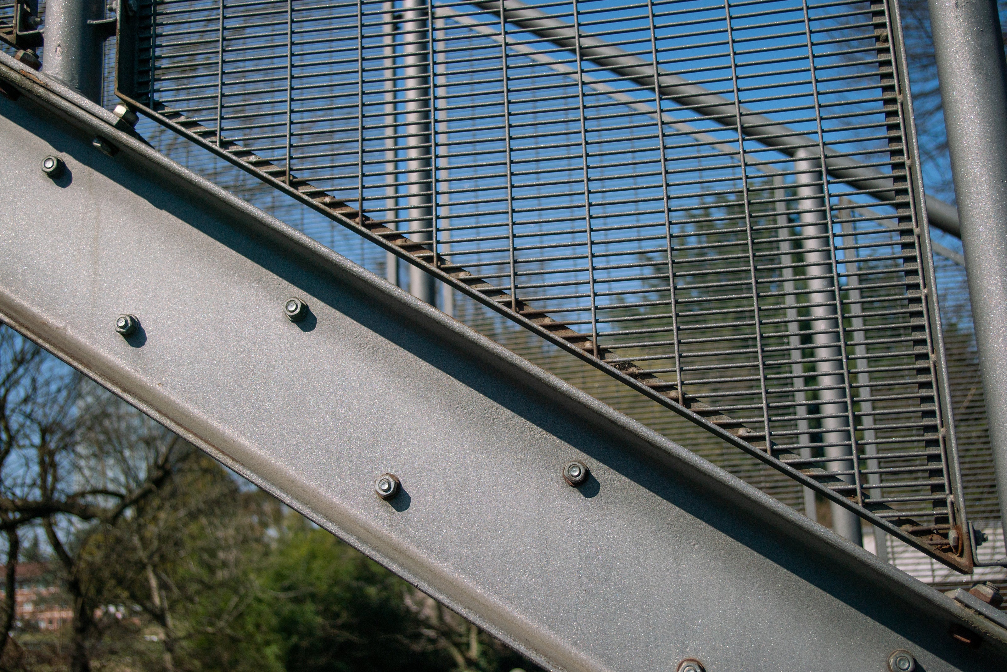 Auf dem Bild ist ein nah rangezoomter Ausschnitt einer Stahlbau-Treppe zu sehen. Man erkennt die Schrauben der Stufen, die Treppenwange und einen Ausschnitt der Geländerfüllung